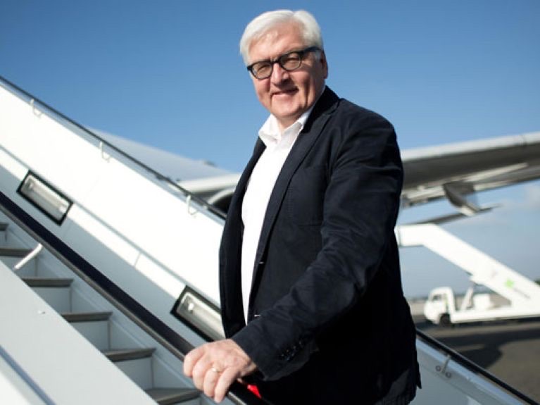 Frank-Walter Steinmeier smiling as he climbs the steps of an aircraft on a sunny day