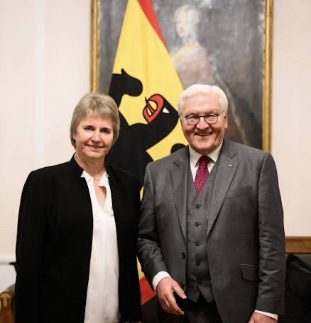 Frank-Walter Steinmeier stands beside a woman in front of a painting and the federal flag