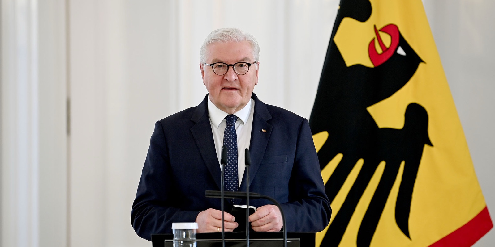 Frank-Walter Steinmeier at a lectern before the yellow federal flag with the black eagle