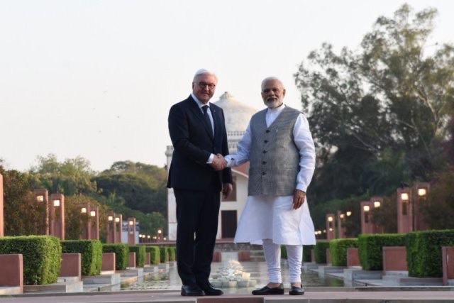 Frank-Walter Steinmeier and Narendra Modi shake hands in a garden at dusk