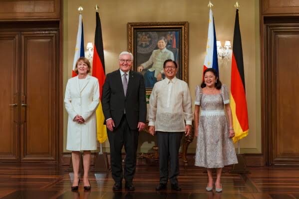 Four people stand in a formal room before Philippine and German flags