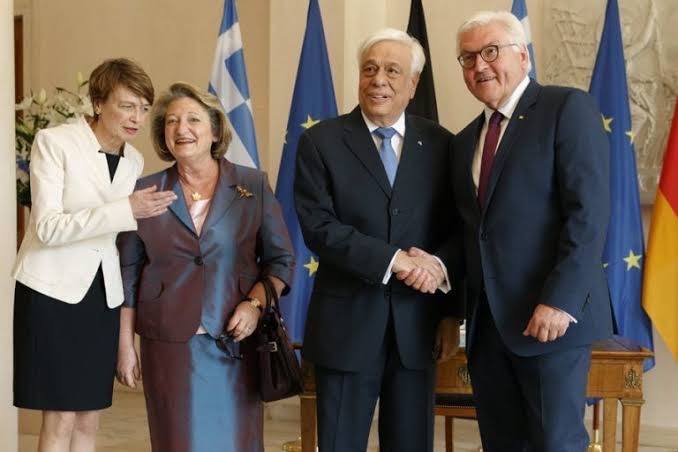 Frank-Walter Steinmeier shakes hands with Greek President Prokopis Pavlopoulos in front of Greek and European flags, with Elke Büdenbender and another woman at left