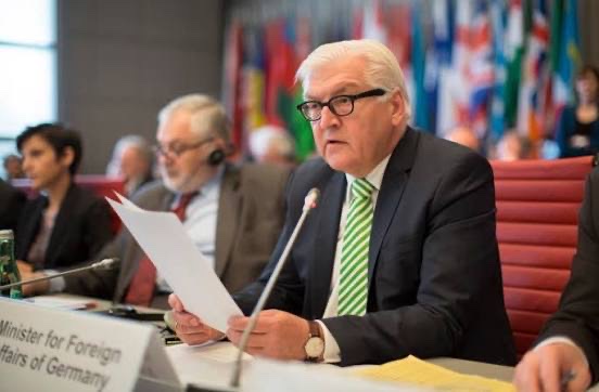Frank-Walter Steinmeier reads a document at a conference table behind a nameplate reading Minister for Foreign Affairs of Germany, with flags behind