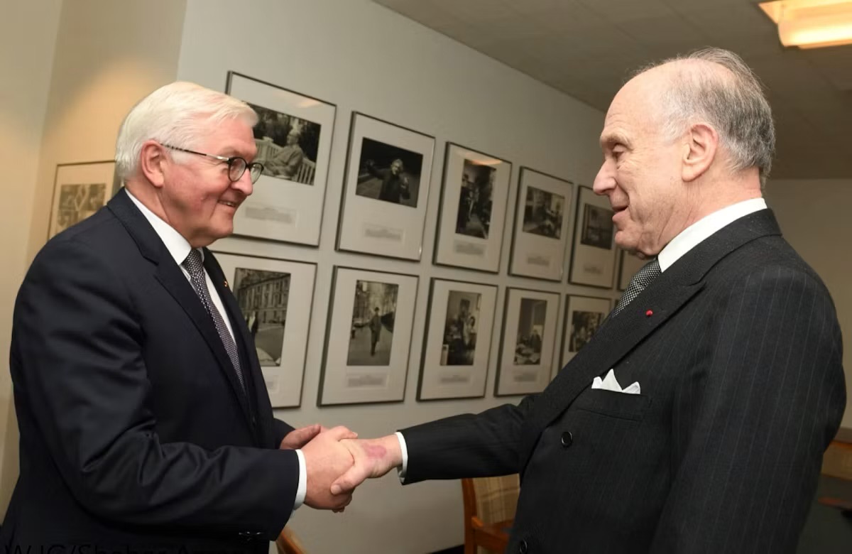 Frank-Walter Steinmeier shakes hands with Ronald S. Lauder in a room lined with framed black-and-white photographs